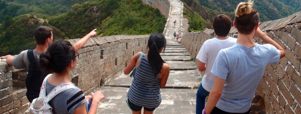 Exchange alumni on the Great Wall of China with their backs to the camera, one student pointing straight ahead